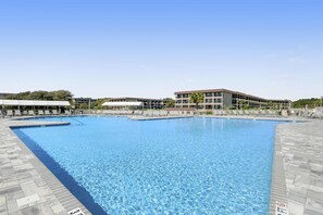 Ein großer rechteckiger Swimmingpool mit klarem, blauem Wasser, umgeben von einer gefliesten Terrasse und einem Gebäude mit mehreren Balkonen im Hintergrund.