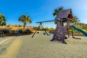 Ein Spielplatz am Sandstrand mit Kletterwand, Schaukeln und Rutsche.