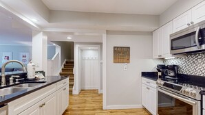 A kitchen with white cabinets, a black countertop, a stainless steel sink, a microwave, and an oven. - Enchanting condo just steps to golf & Harbour Town Marina (Hilton Head)
