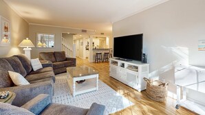 A modern living room with a sofa set, a coffee table, a TV, and a kitchen area in the background. - Enchanting condo just steps to golf & Harbour Town Marina (Hilton Head)