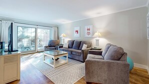 A modern living room with a grey sofa set, a glass coffee table, and a patterned rug. - Enchanting condo just steps to golf & Harbour Town Marina (Hilton Head)
