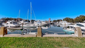 A marina with various boats docked, a lighthouse in the background, and a grassy foreground. - Enchanting condo just steps to golf & Harbour Town Marina (Hilton Head)