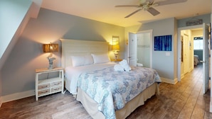 A bedroom with a bed, bedside lamps, a nightstand, a ceiling fan, and a hallway leading to another room. - Coastal condo- close to Coligny Plaza, Beach with shared pool (Hilton Head)