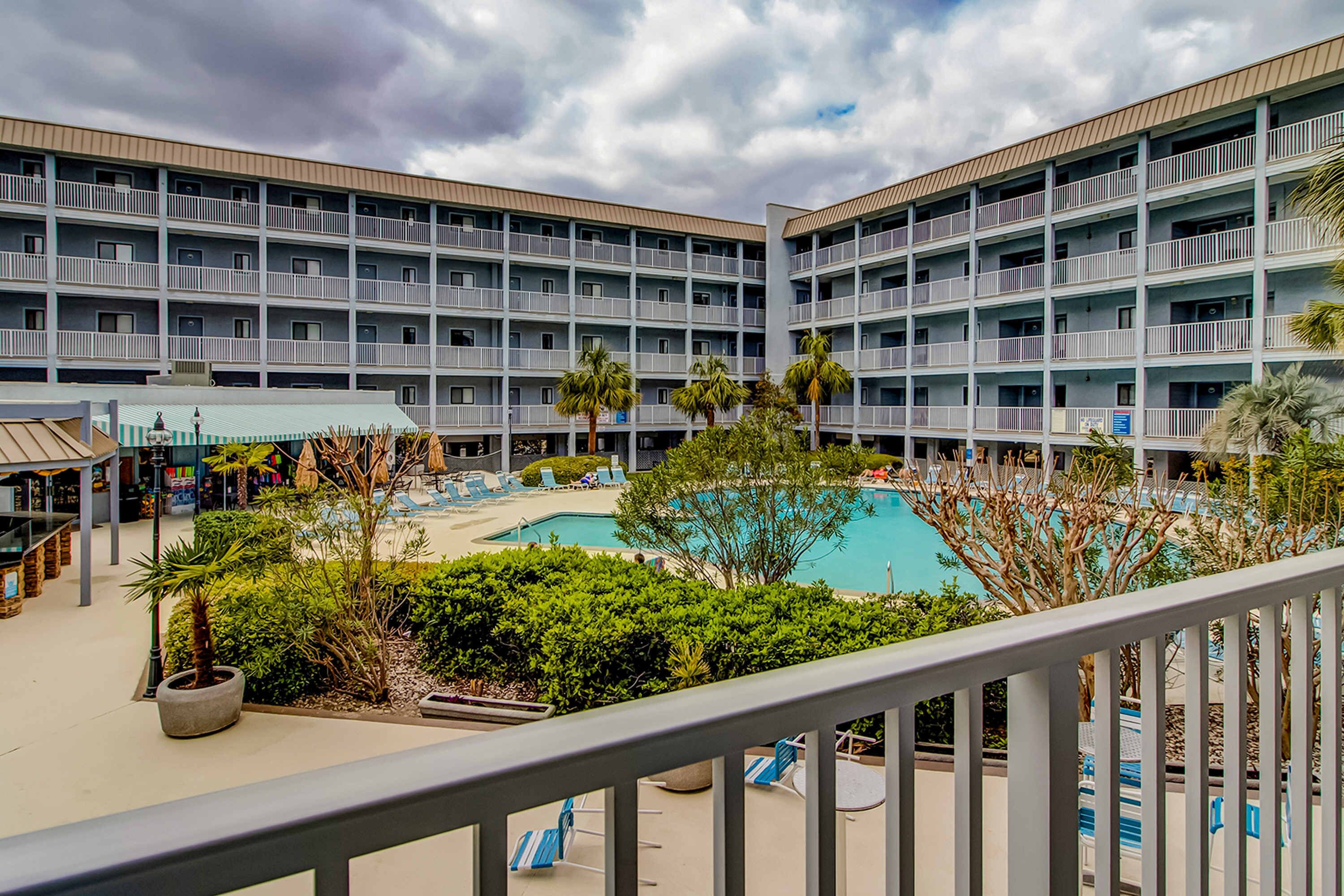 A hotel with multiple balconies, a swimming pool, and a landscaped area with palm trees.