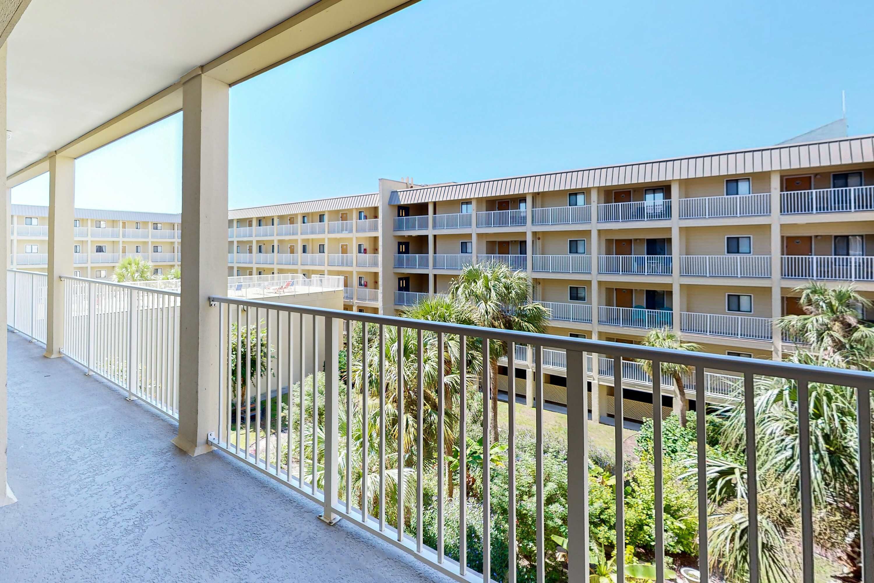 Un hotel de diversos pisos amb balcons, un pati amb palmeres i un cel blau clar.