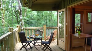 A wooden deck with a table and chairs, a small table with a plant, and a view of the forest.