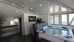 A spa room with a hot tub, a shower area, and a window with blinds.