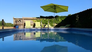 A swimming pool with a green umbrella, lounge chairs, and a wooden structure in the background.