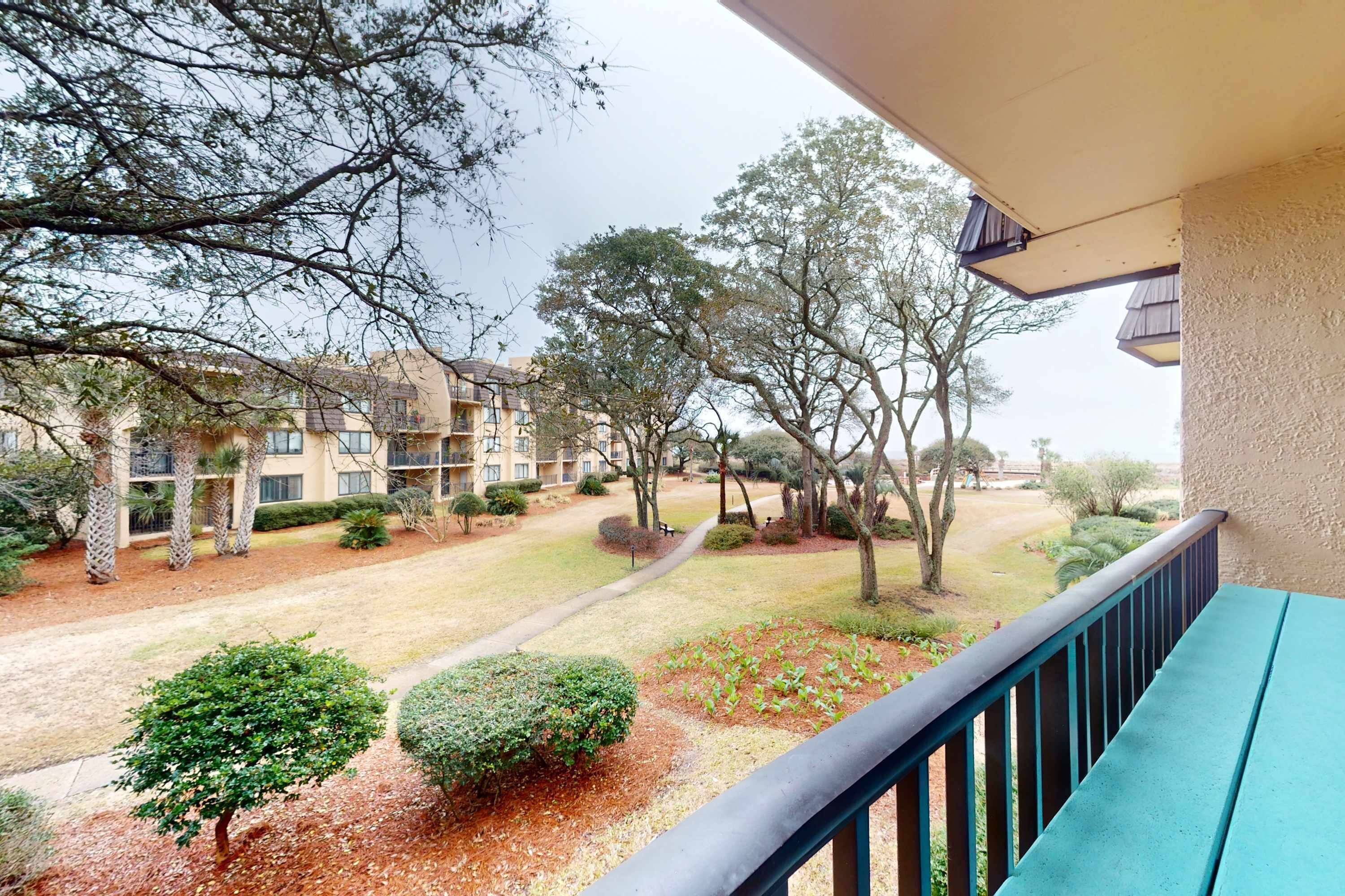 A balcony with a view of a courtyard, including a pathway, trees, and a building in the background.