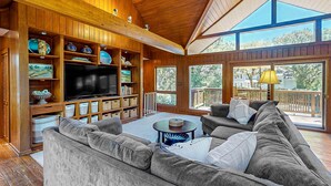 Ein geräumiges Wohnzimmer mit großem Flachbildfernseher, Holzböden und einer gemütlichen Sitzecke.