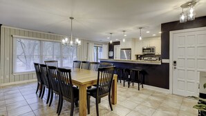 A modern kitchen with a dining area, featuring a wooden table and chairs, a bar counter, and a refrigerator. - Breezy resort home located in Sea Pines Resort near marina & restaurants (Hilton Head)