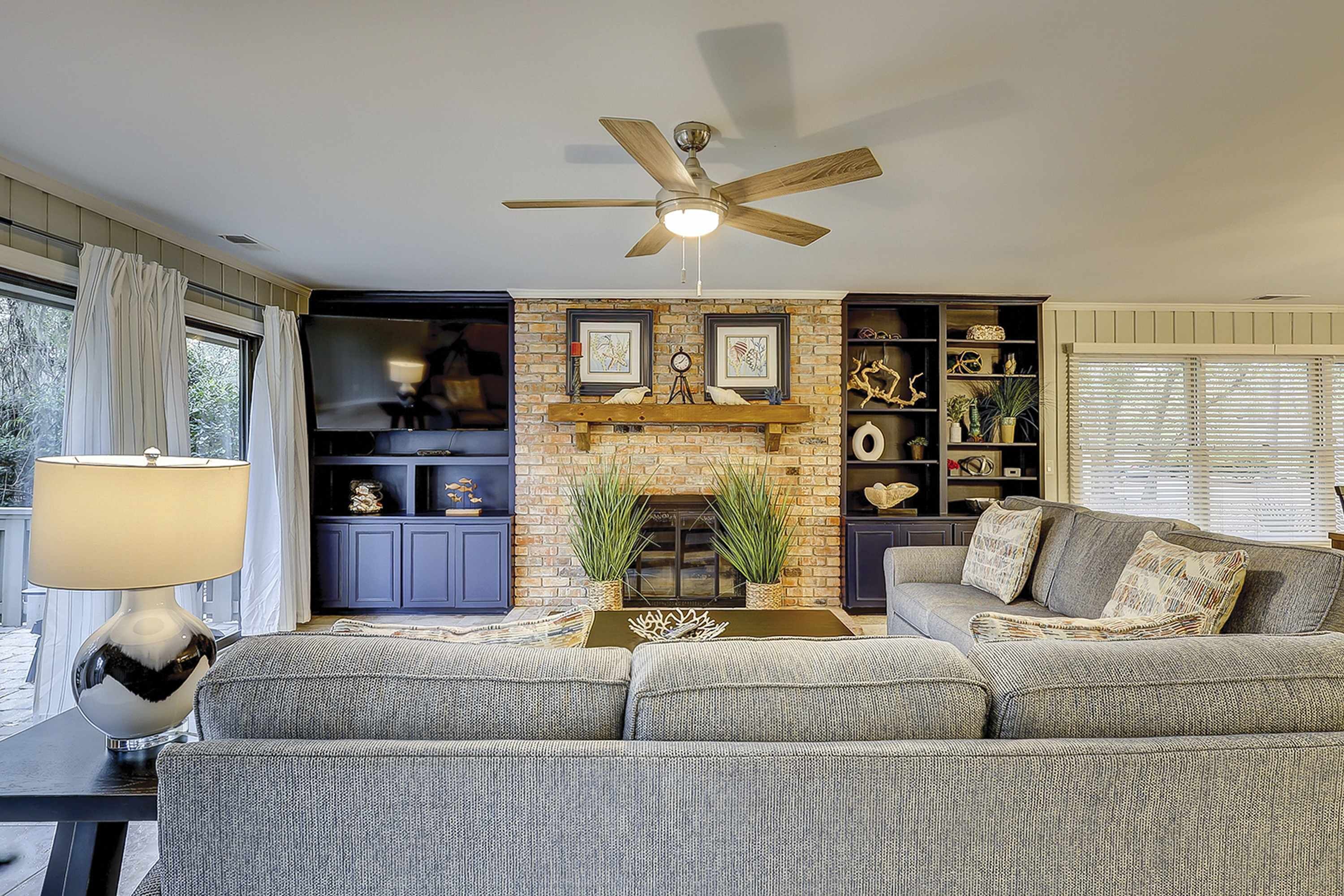 A living room with a sofa, a fireplace, a ceiling fan, and a lamp.