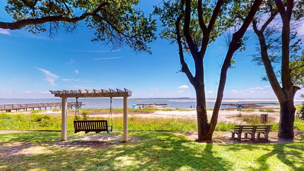 Un parque con un pérgola de madera, bancos y vistas a la playa y el océano.