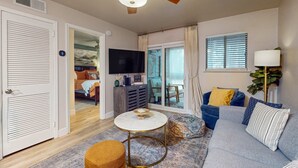 Sala de estar con ventilador de techo, televisor de pantalla plana, sofá, mesa de centro y vistas al exterior.