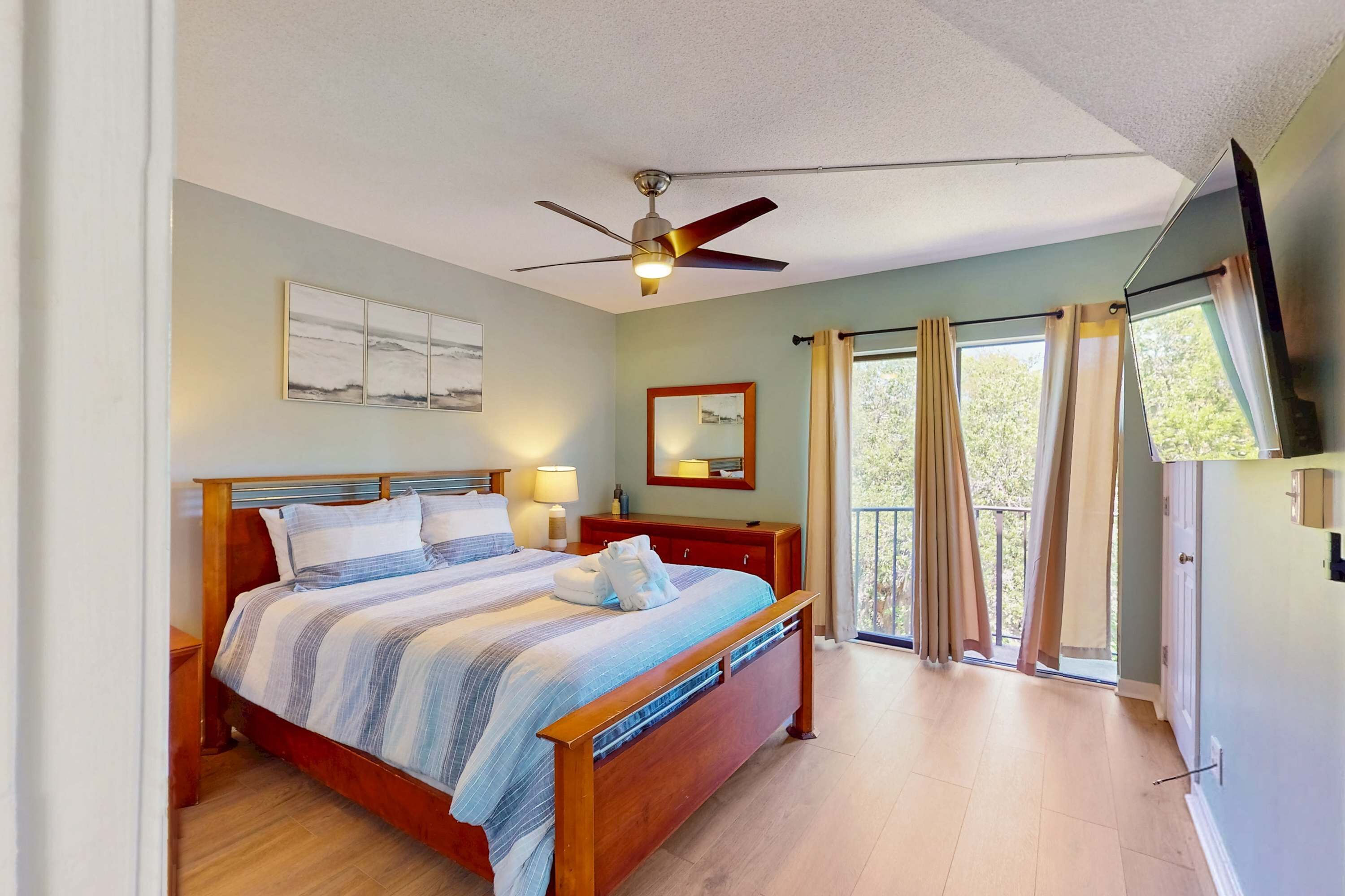 Un dormitorio con cama, ventilador de techo, televisión, ventana con cortinas y balcón.