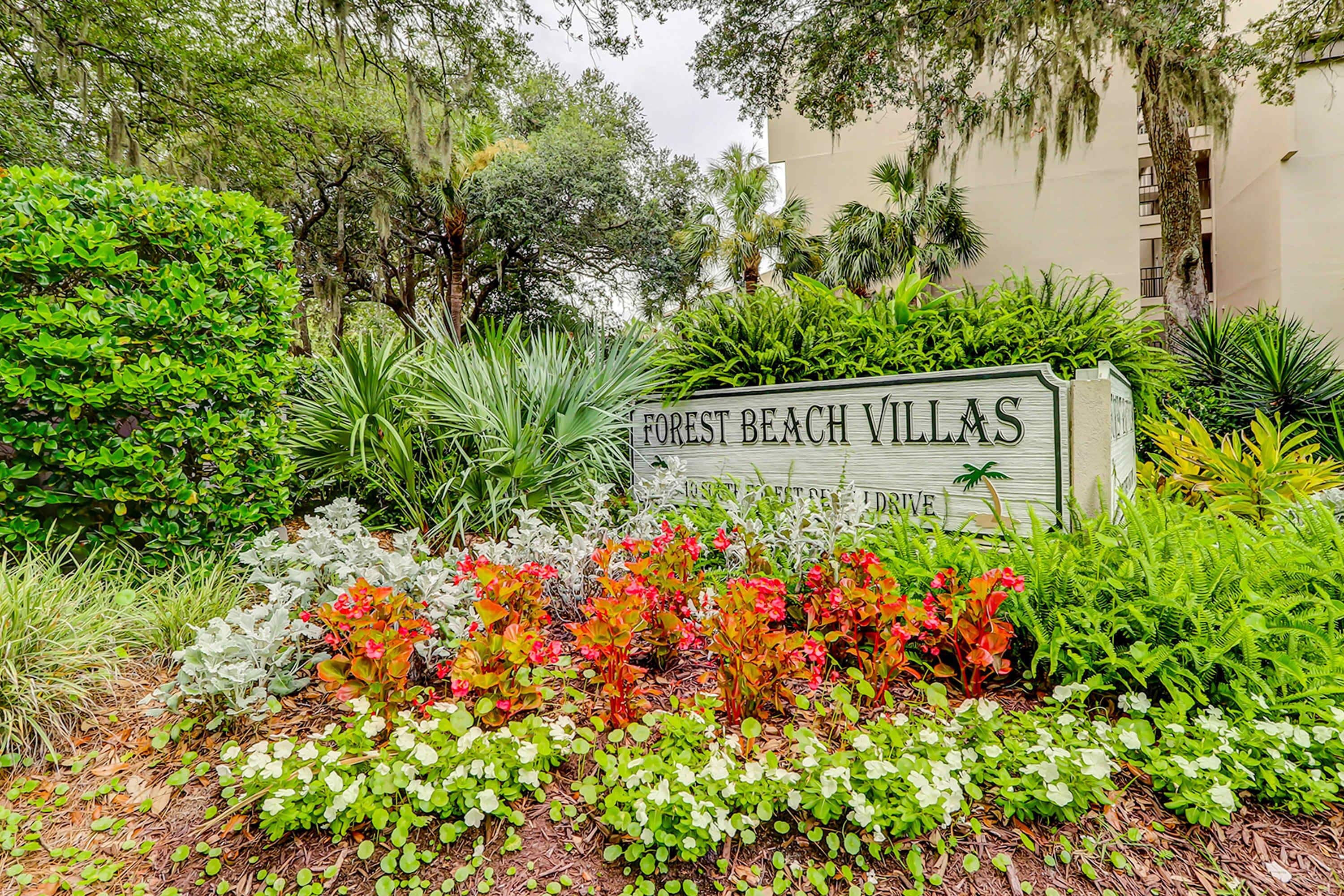 Skilt for 'Forest Beach Villas' omgivet af frodigt grønt og diverse planter.