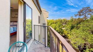 Ein Balkon mit Blick auf einen Wald, ein Bett und ein Sessel.