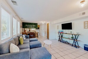 Uma sala de estar com um sofá, uma mesinha e uma cozinha ao fundo.