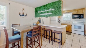 A kitchen with a white countertop, wooden chairs, a hanging green wall decoration, and a microwave. - Spacious house by the beach with screened balcony & central AC (Hilton Head)