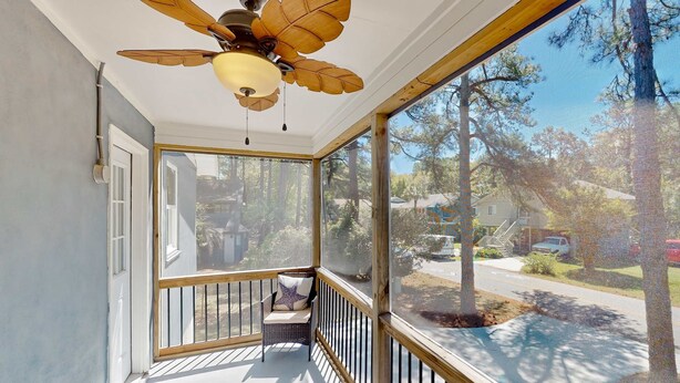 A covered porch with a ceiling fan, a chair with a cushion, and a view of a residential street. - Spacious house by the beach with screened balcony & central AC (Hilton Head)