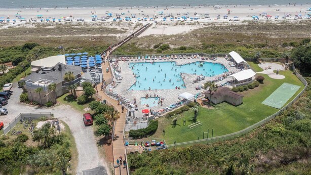 Vista aérea de um resort com uma piscina central, vários guarda-sóis de praia e uma área de praia.