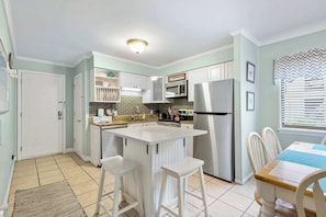 A kitchen with white cabinets, a central island, stainless steel appliances, and a dining area with a table and chairs. - Condo near beach with 2 pools, restaurants, gym, 6 tennis, 12 pickleball, W D (Hilton Head)
