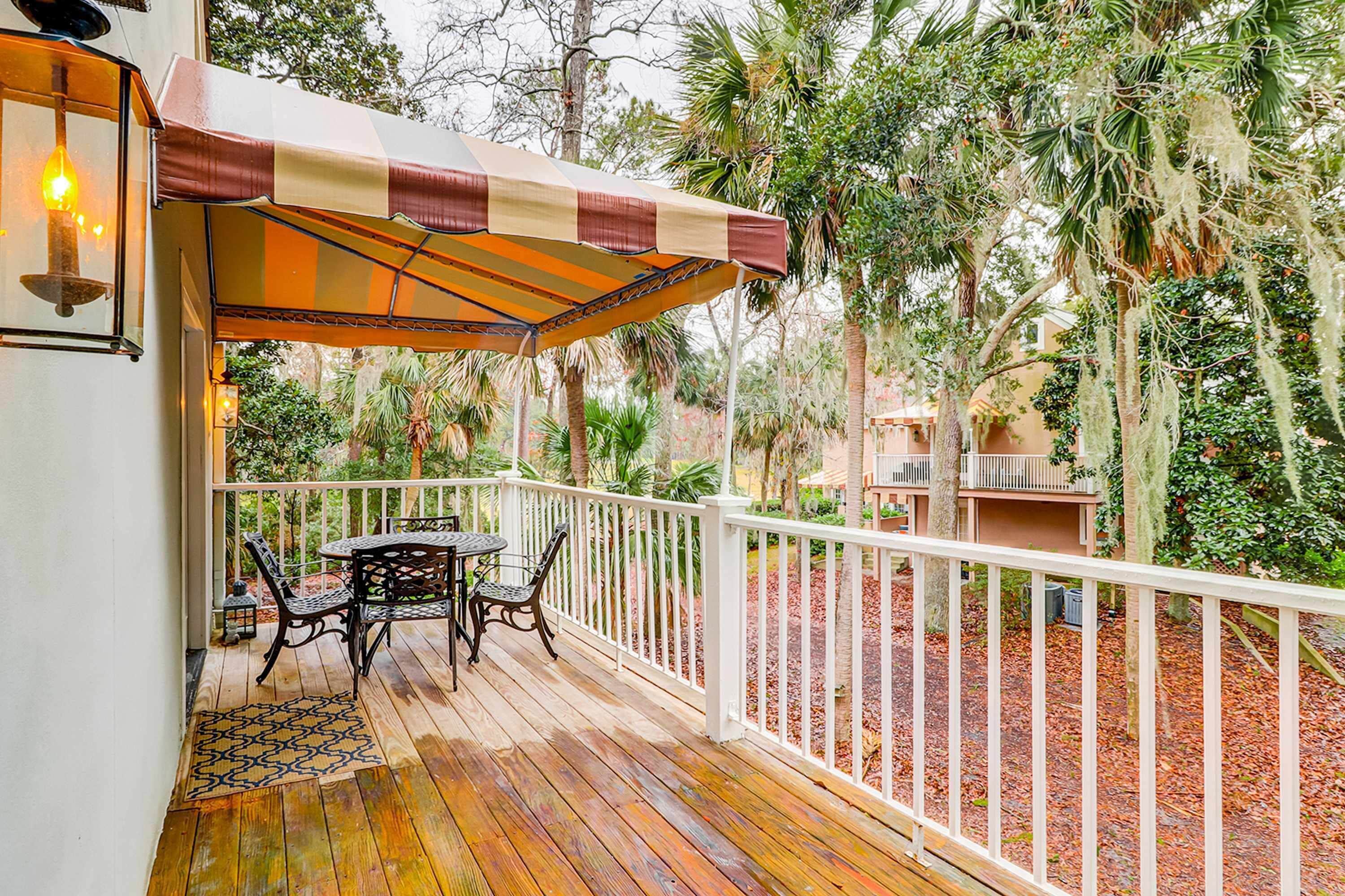 A wooden deck with a table and chairs, a striped awning, and a white railing.