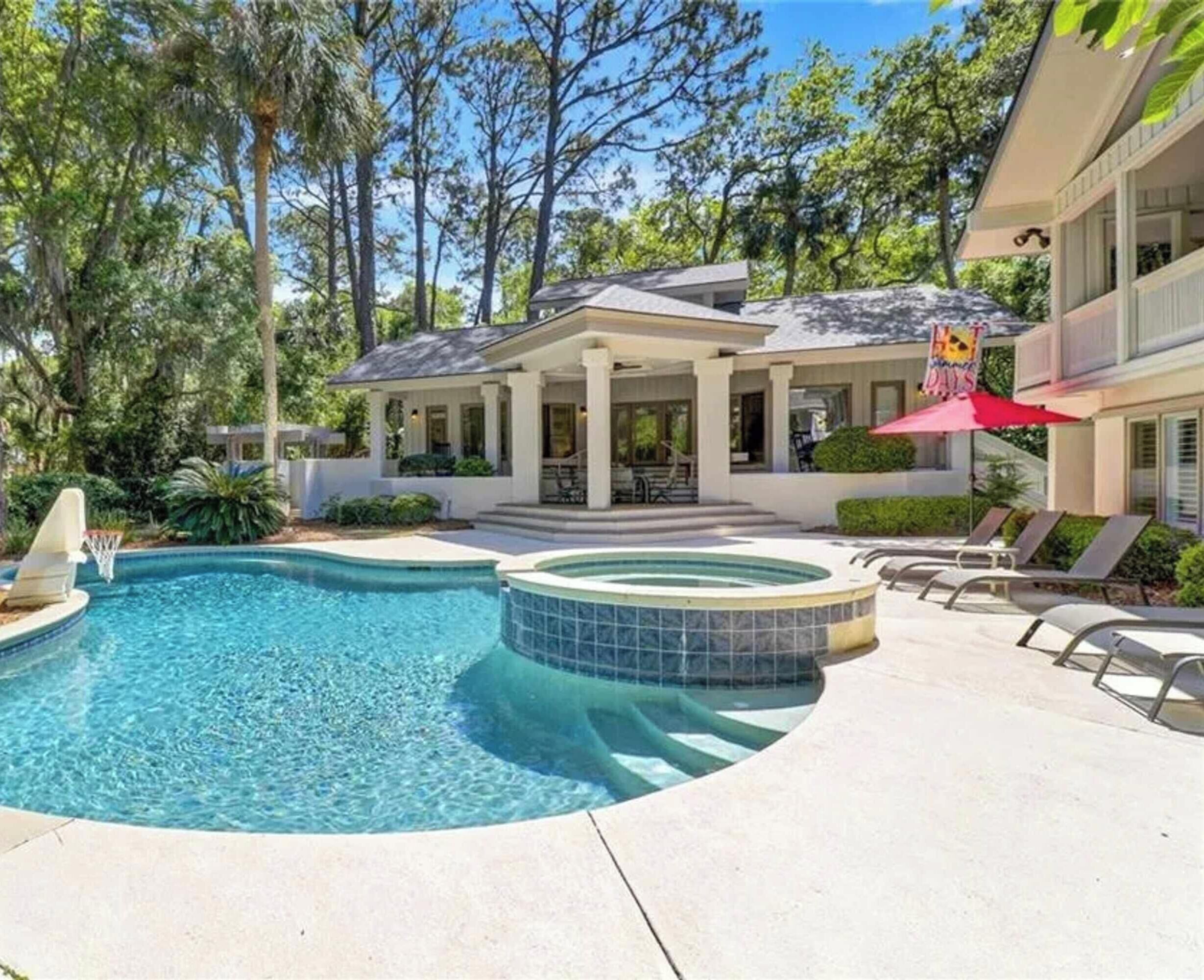 A swimming pool with a hot tub, lounge chairs, and a covered patio area.