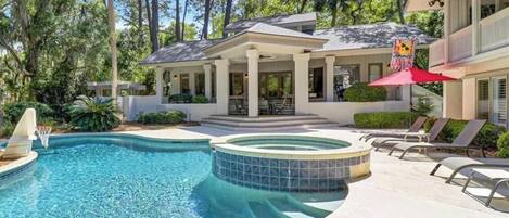 A swimming pool with a hot tub, lounge chairs, and a covered patio area.