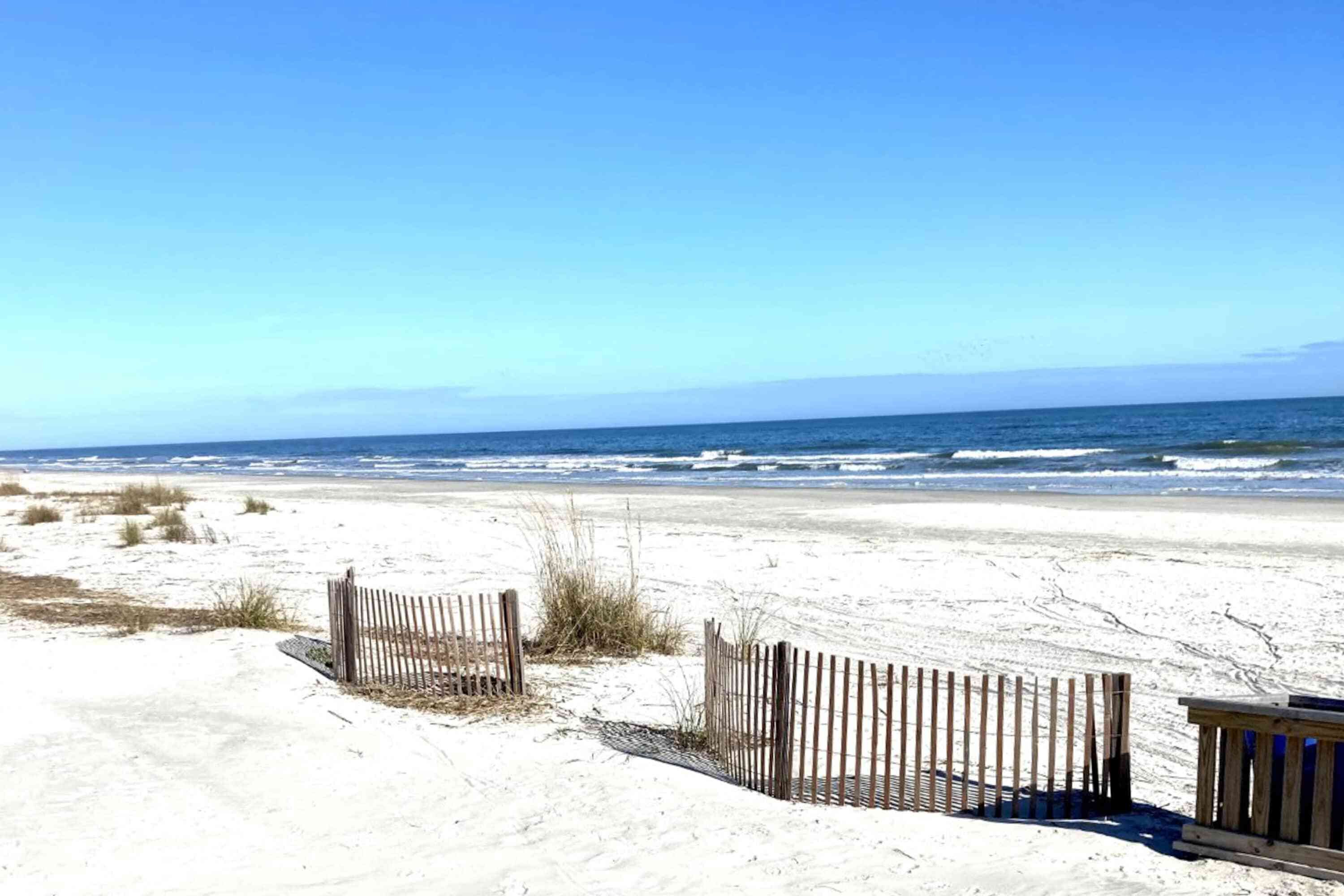 Ein Sandstrand mit einer Holzlattenverkleidung und einer Holzhütte unter blauem Himmel.