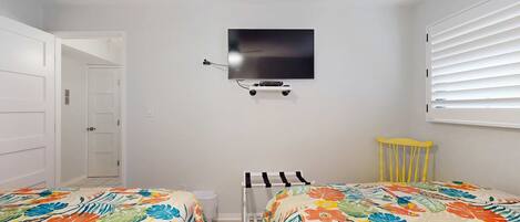 A bedroom with two beds, a ceiling fan, a TV mounted on the wall, and a window with blinds.