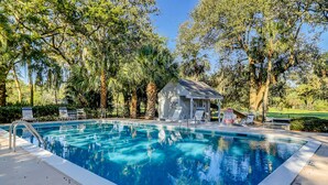 Une piscine avec un plongeoir, entourée d’arbres et agrémentée d’un petit kiosque.
