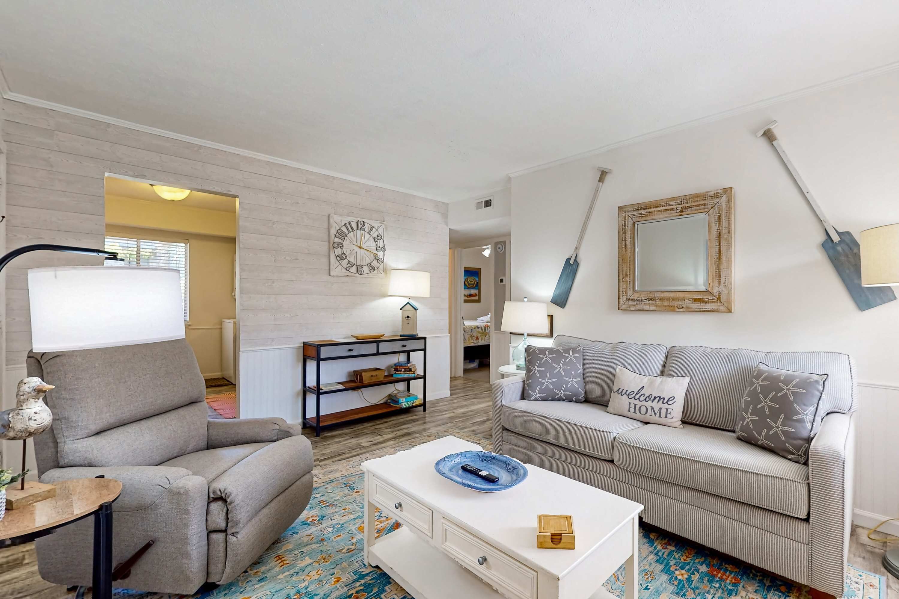 Una sala de estar con sofá, mesa de centro, lámpara, estantería y un reloj de pared.