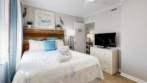 A bedroom with a bed, a television, a ceiling fan, a door, and a small white dresser. - Relaxing condo with heated chilled pool, easy beach access, patio, & W D (Hilton Head)