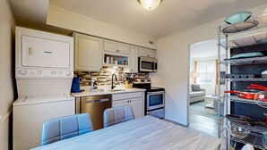 A compact kitchen with white cabinets, a microwave, an oven, and a dining table with chairs. - Relaxing condo with heated chilled pool, easy beach access, patio, & W D (Hilton Head)