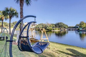 Una cadira-bressol a la vora d'un llac, amb un balancí de fusta i una casa al fons.