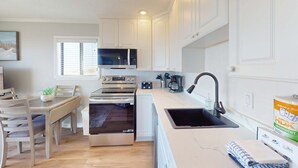 A modern kitchen with white cabinets, a microwave, an oven, a sink, and a dining area with a table and chairs. - 1st floor condo near the beach with pool, tennis, balcony, gym, streaming, WD (Hilton Head)