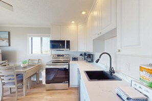 Una cuina moderna amb armaris blancs, un microones, un forn, un rentamics i una zona de menjador amb taula i cadires.