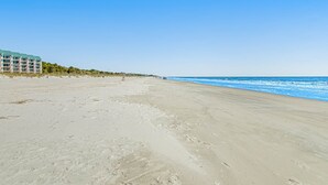 A beach with a building on the left, clear skies, and ocean waves. - 1st floor condo near the beach with pool, tennis, balcony, gym, streaming, WD (Hilton Head)