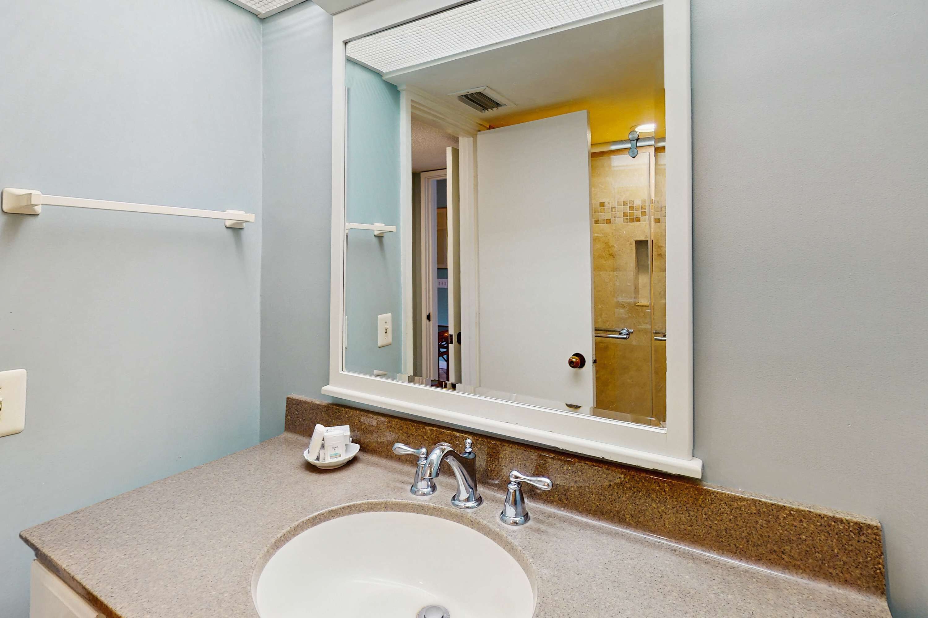 Un bagno con un lavandino bianco, due rubinetti, un portasciugamani e uno specchio che riflette una porta e un’area doccia.
