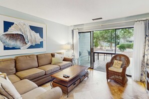 Una sala de estar con un sofá, una mesa de centro, un sillón de mimbre y un ventanal con vistas al exterior.