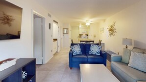 A living room with a blue sofa, a white coffee table, and a grey sofa. There is a dining area in the background with a table and chairs. - Coastal Retreat with Patio, Shared Pools, Tennis & Playground - Walk to Beach (Hilton Head)