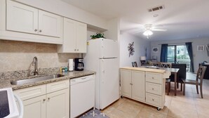A kitchen with white cabinets, a refrigerator, a coffee maker, and a dining area with a table and chairs. - Coastal Retreat with Patio, Shared Pools, Tennis & Playground - Walk to Beach (Hilton Head)