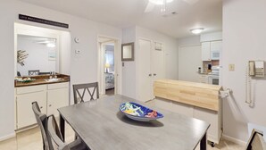 A dining area with a wooden table, chairs, a decorative bowl, a ceiling fan, and a kitchen in the background. - Coastal Retreat with Patio, Shared Pools, Tennis & Playground - Walk to Beach (Hilton Head)