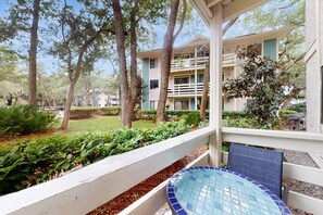 A covered outdoor area with a tiled pool table, a white railing, and a building with multiple balconies in the background. - Coastal Retreat with Patio, Shared Pools, Tennis & Playground - Walk to Beach (Hilton Head)