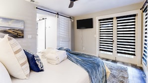 Ein Schlafzimmer mit einem Bett, einem Deckenventilator, einem Fernseher und einer Schiebetür.