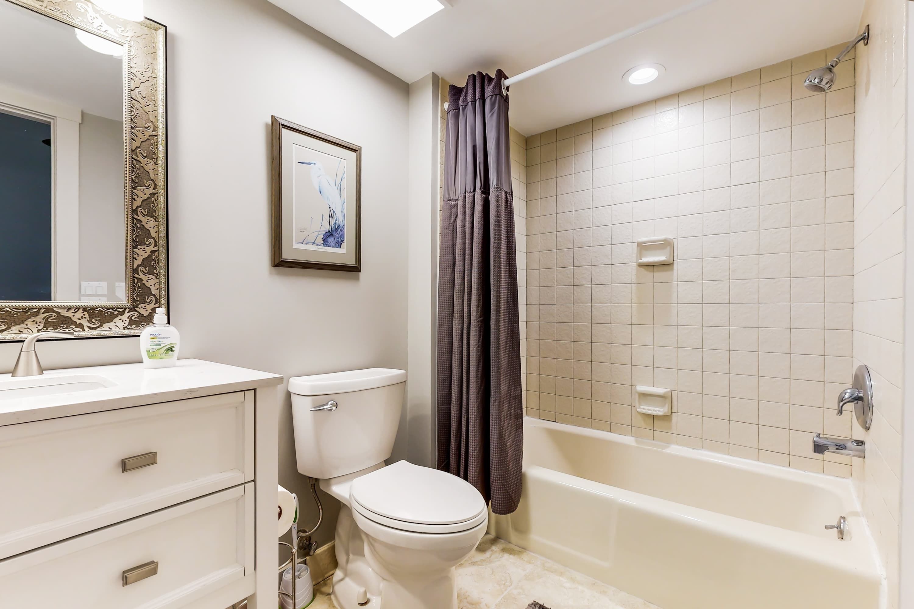 A bathroom with a toilet, sink, mirror, shower curtain, and bathtub.
