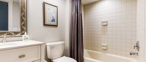 A bathroom with a toilet, sink, mirror, shower curtain, and bathtub.
