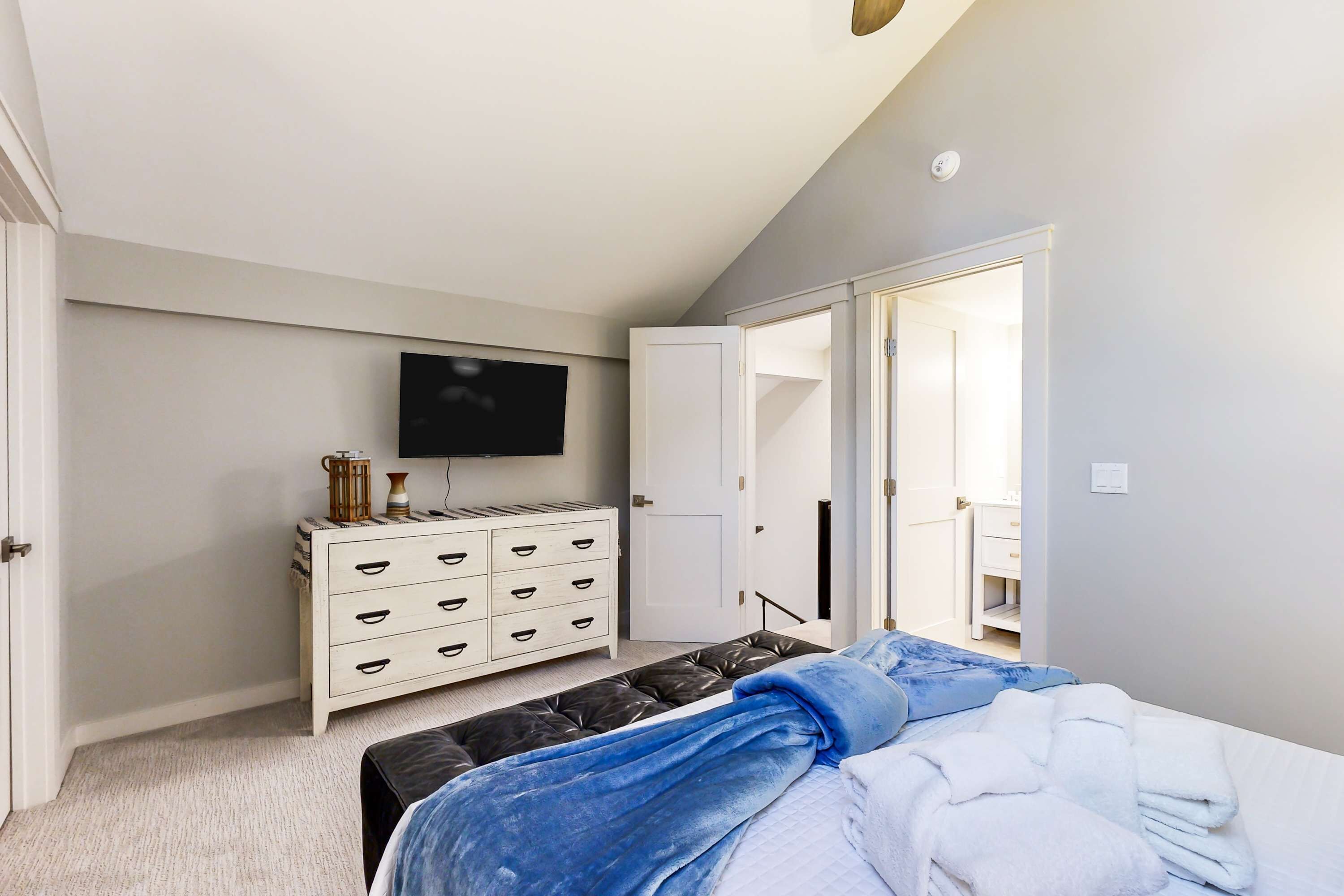 Een slaapkamer met een bed, een televisie, een dressoir en een deur die leidt naar een balkon.