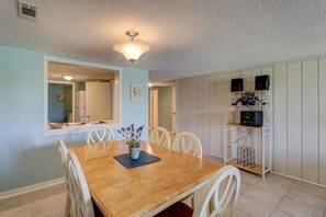 A dining area with a wooden table, white chairs, a potted plant, and a wall-mounted shelf with speakers. - Sea Pines condo with amazing golf course view, pool, & balcony - walk to beach (Hilton Head)